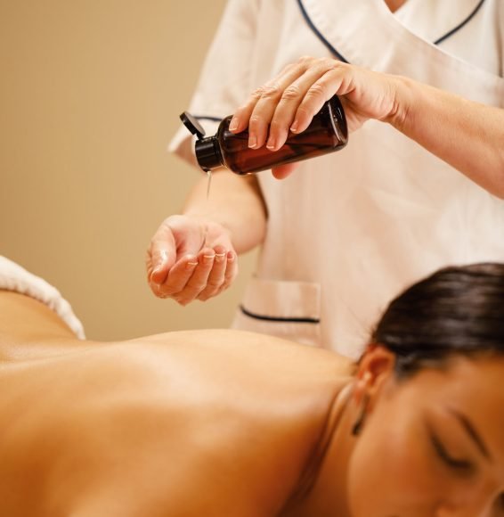 Unrecognizable therapist pouring oil in her hands before massage treatment at the wellness center,